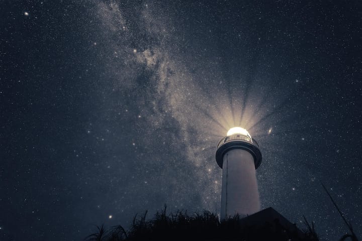 Lighthouse shining under a starry night sky with the Milky Way