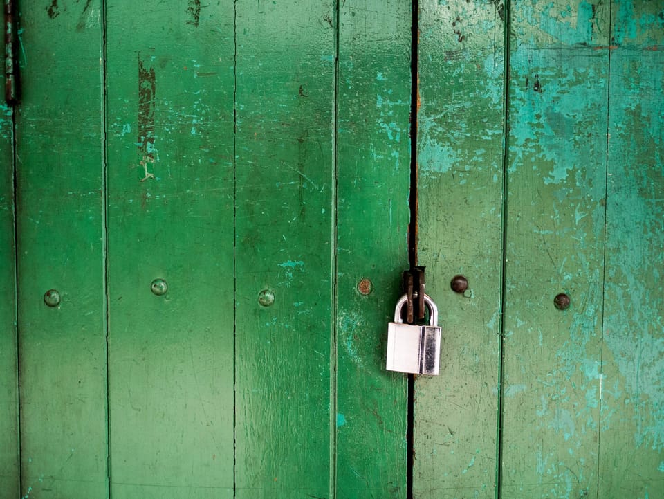 Green wooden door locked with a padlock