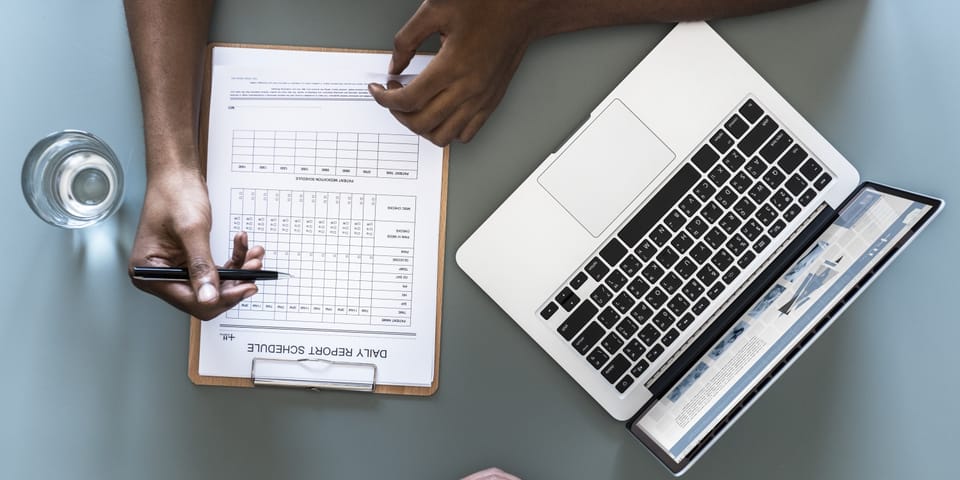 Doctor writing notes on a clipboard next to a laptop